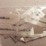 mittig gefaltene Textiletiketten mit dem Aufdruck 100% Baumwolle und Pflegesymbole 10mm schmahl.