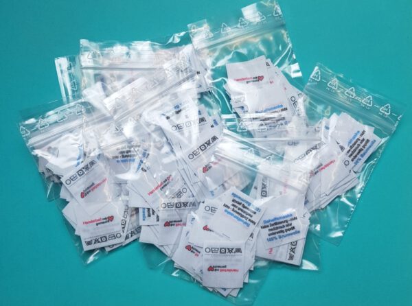 Handarbeit, 100% Baumwolle, Behelfsmaske, Pflege 60° X 1 1 O, Mittelfalte mittig gefaltene Labels mit Aufdruck wie abgebildet. Baumwoll-Mischband, weiß : 25 x 27mm; Fertigmaß nach Mittelfalte: 25 x 27mm.