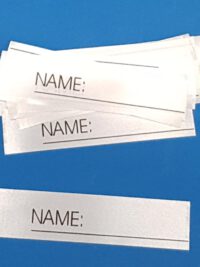 25 Stück Textiletiketten mit Aufdruck "Name_______" zum Beschreiben einzeln geschnitten.   |   Abmessungen: 15x63mm  (+/- 1mm) ENR: links   |   ENR = Einnähraum Zusammensetzung Band: 100% Polyester (Satinband)