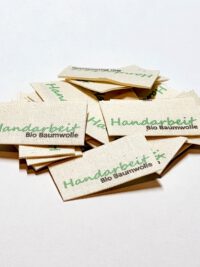 Textiletiketten aus Naturbaumwollband mit der Aufschrift in grün "Handarbeit"