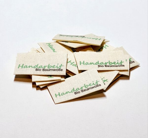 Textiletiketten aus Naturbaumwollband mit der Aufschrift in grün "Handarbeit"